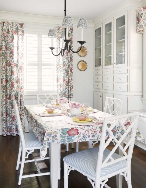 raňajková miestnosť, biele jedálenské stoličky, bielo -modré vyzliekané podsedáky, biely úložný priestor, kvetinové závesy a doska stola
