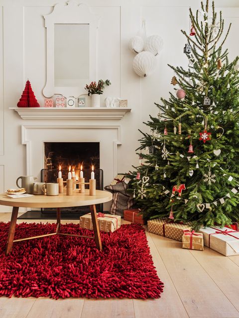 brad de Crăciun în colțul unei camere de zi cu un covor roșu mare sub o masă rotundă din lemn și un foc răcnitor în fundalul stilului scandi covorul superb oferă o cale minunată de a aduce un element de culoare în a ta