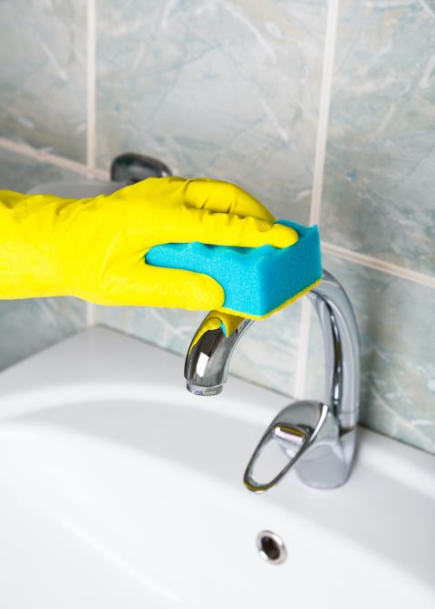 pandemični dezinfekcijski človek v rumenih rokavicah čisti kopalniško pipo in služkinja za kopel in umivalnik v rumenih zaščitnih rokavicah umiva umazano kopalno pipo ali umivalnik roke umiva ali čisti kopel od blizu
