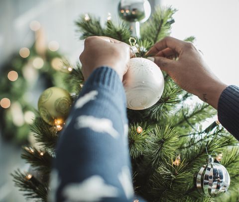 Mladý muž oslavujúci Vianoce doma a zdobenie vianočného stromčeka doma je ozdobený vianočnými ozdobami a svetlami