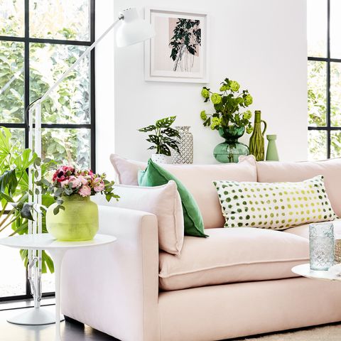 ružová pohovka v bielej miestnosti so zelenými rastlinami okolo a zelenými vzorovanými vankúšmi