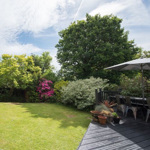 splošen pogled na zadnji vrt s sivim pokrovom z vrtno mizo in stoli na sončen dan v domu